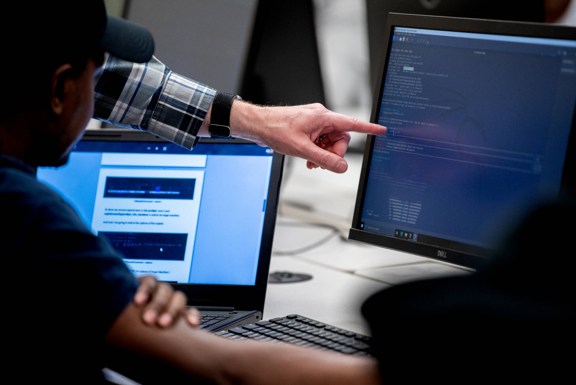 students sitting down pointing at their computer screens that show code
